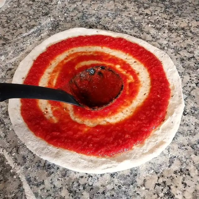 La sauce tomate étalée à la louche sur la pâte